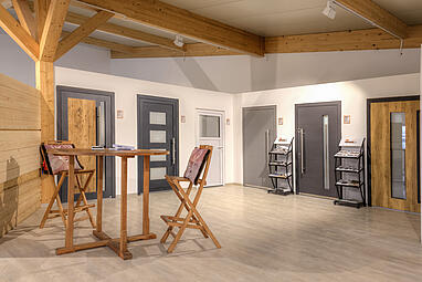 Moderner Ausstellungsraum der Schwabenholz GmbH mit Holzelementen, Türen in verschiedenen Designs und einem kleinen Stehtisch mit Stühlen.