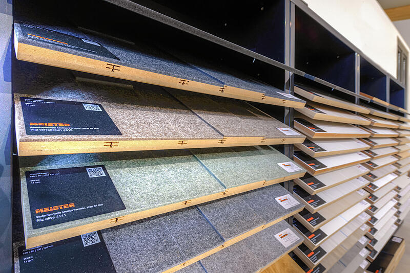  Ausstellung von Teppichmustern in schrägen Regalen in einem Teppich- oder Bodenbelagsgeschäft mit verschiedenen Farben und Texturen.