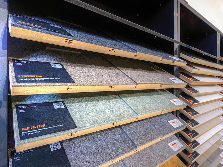  Ausstellung von Teppichmustern in schrägen Regalen in einem Teppich- oder Bodenbelagsgeschäft mit verschiedenen Farben und Texturen.
