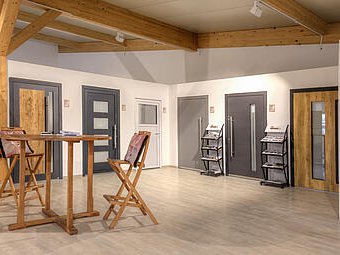 Moderner Ausstellungsraum der Schwabenholz GmbH mit Holzelementen, Türen in verschiedenen Designs und einem kleinen Stehtisch mit Stühlen.